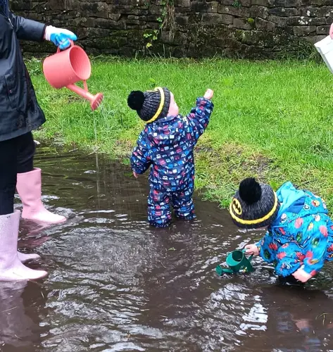 Two toddlers in puddle suits playing in the rain and puddles