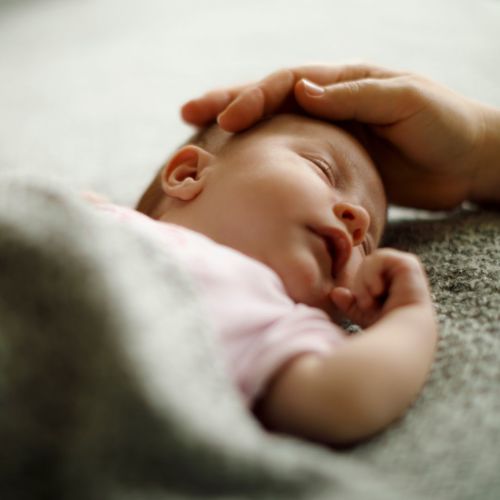 A baby sleeping with their head being gently stroked by a parent