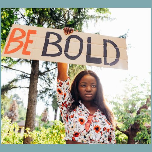 A black woman holding a placard saying Be Bold